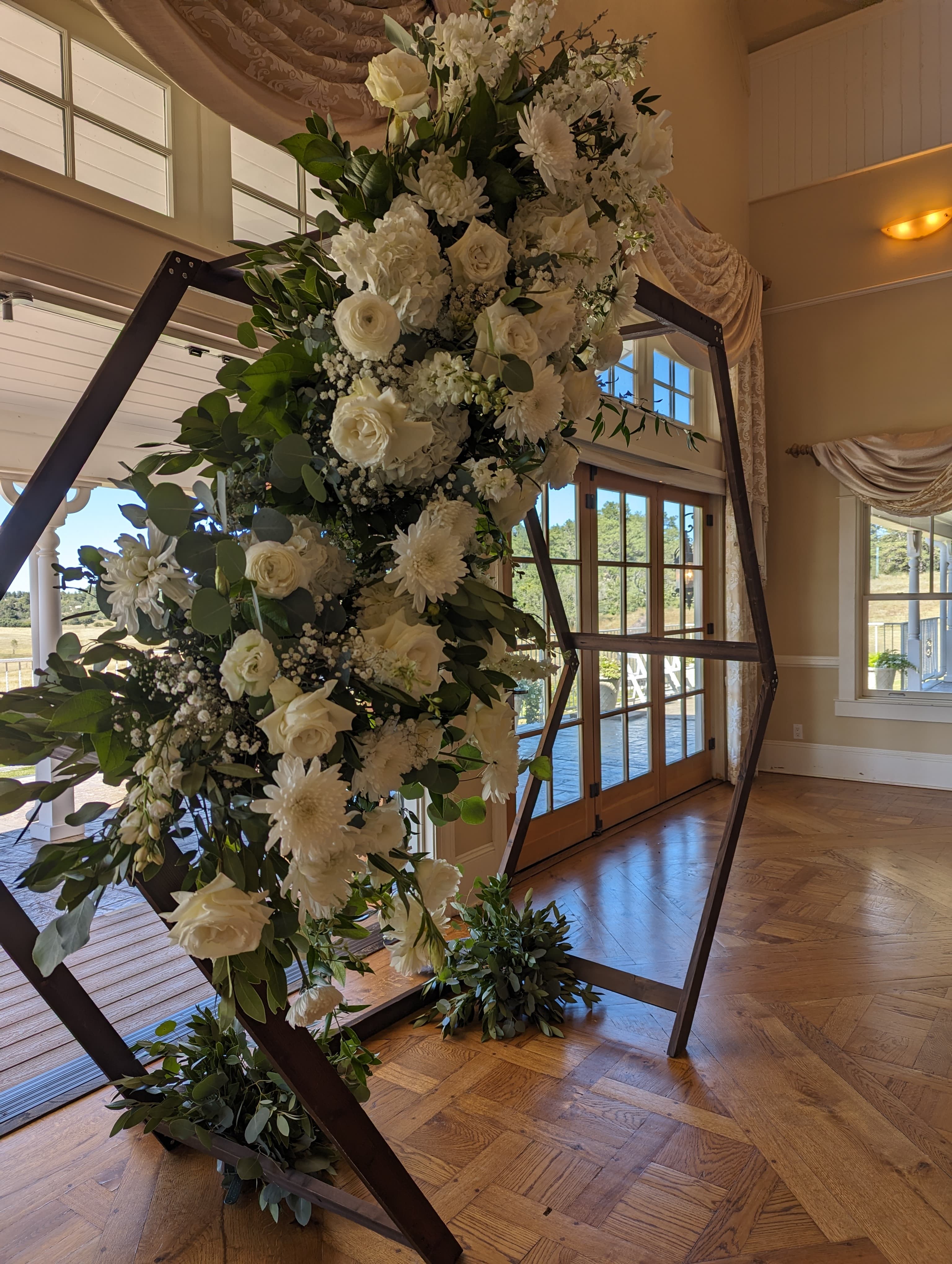 Hexagonal arch frame with cascading white roses, dahlias, and eucalyptus in an elegant venue with herringbone floors